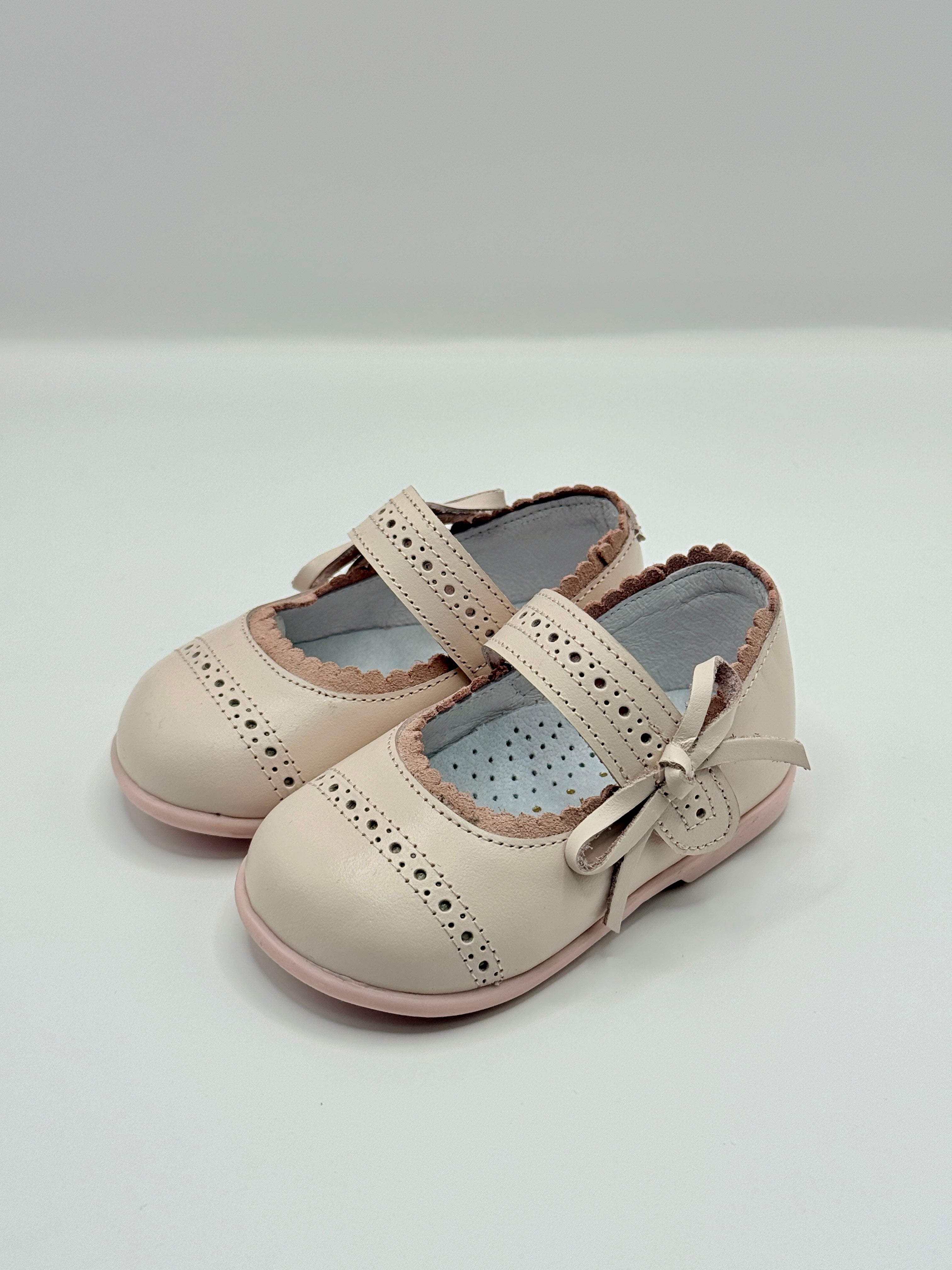 Pair of beige children's shoes with a bow on a white background
