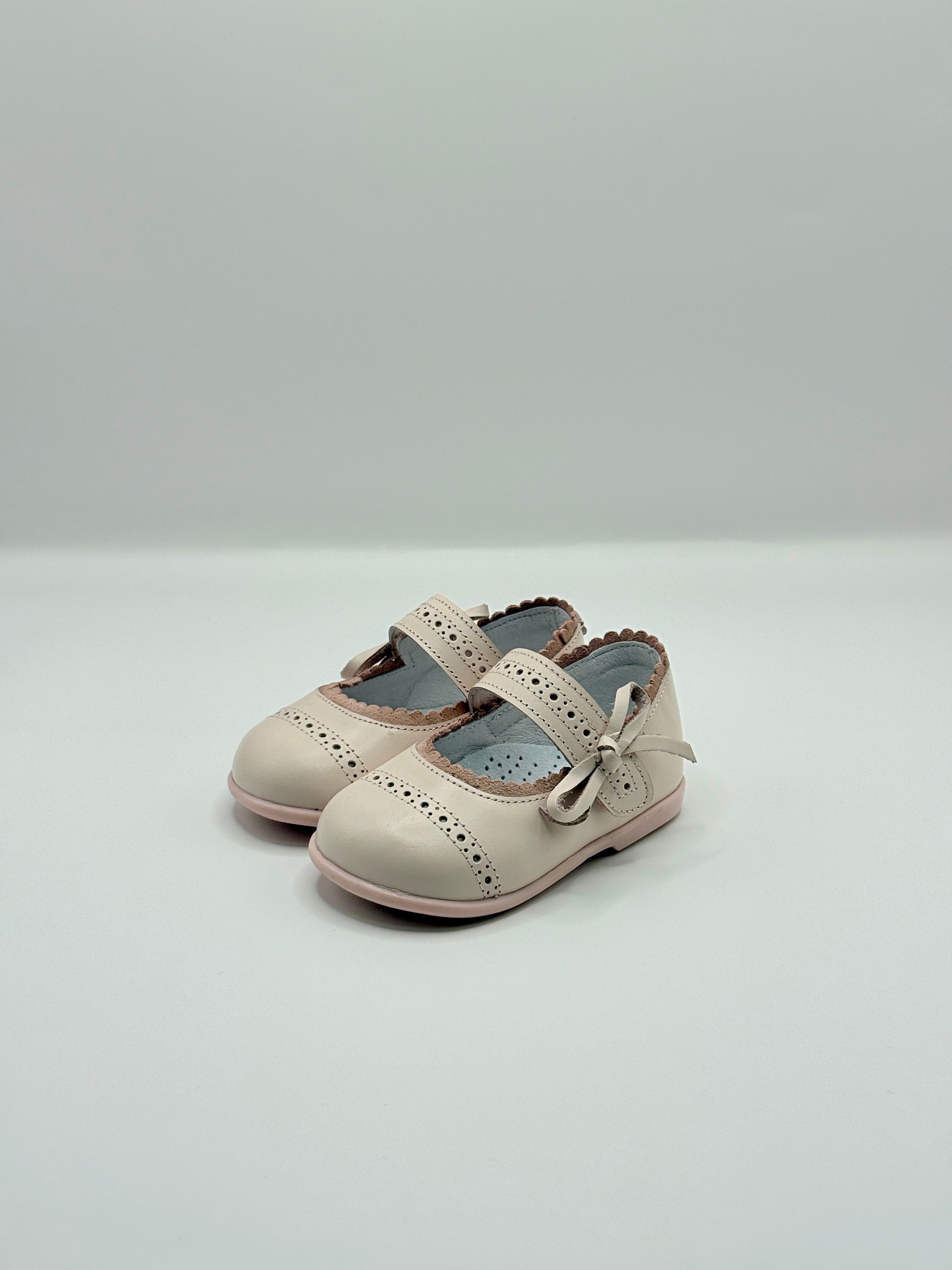 Pair of light pink children's shoes with a bow on a white background