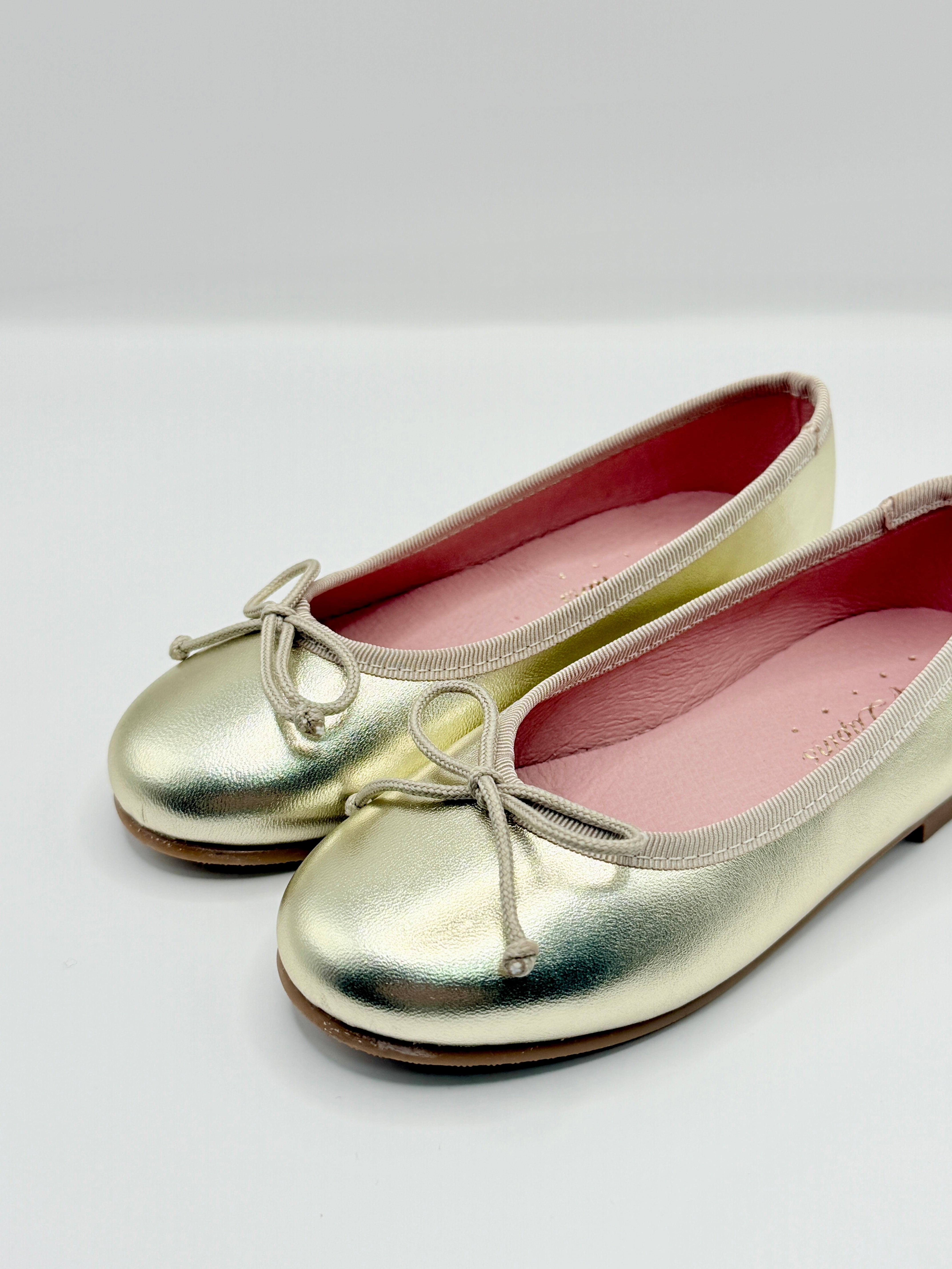Pair of metallic gold shoes with pink interior on a white background