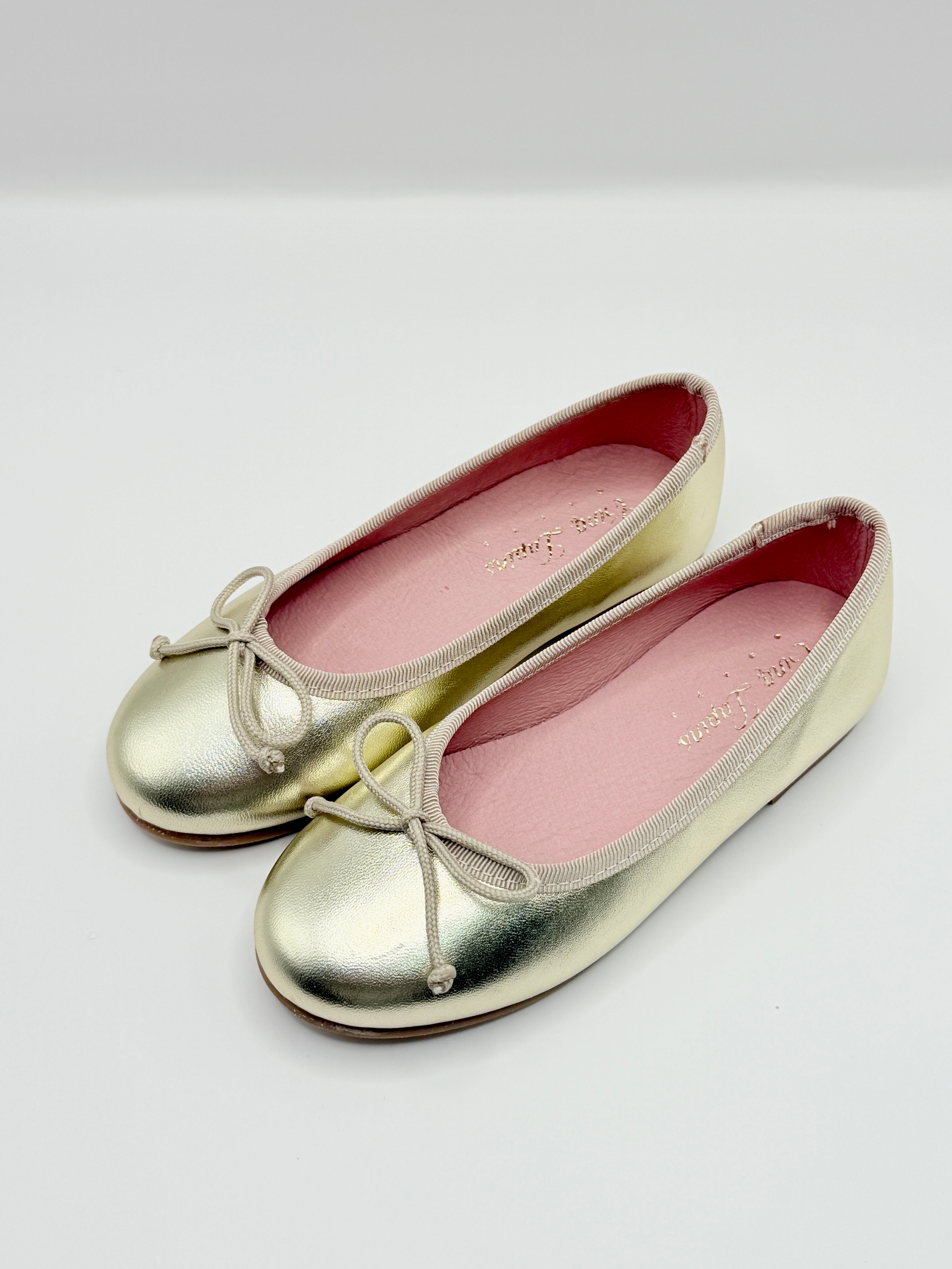 Pair of metallic gold shoes with pink interior on a white background