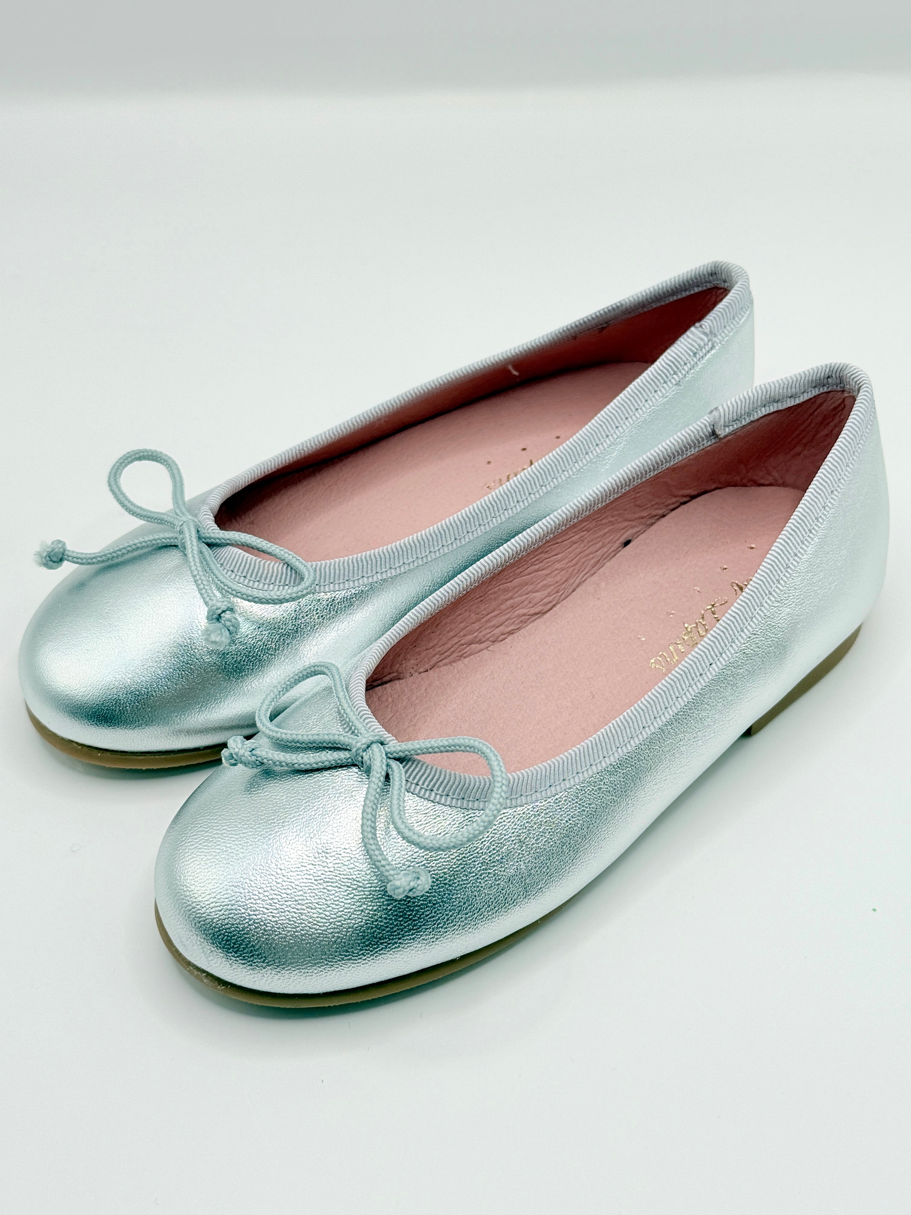 Silver metallic ballet flats with bow details on a light gray background