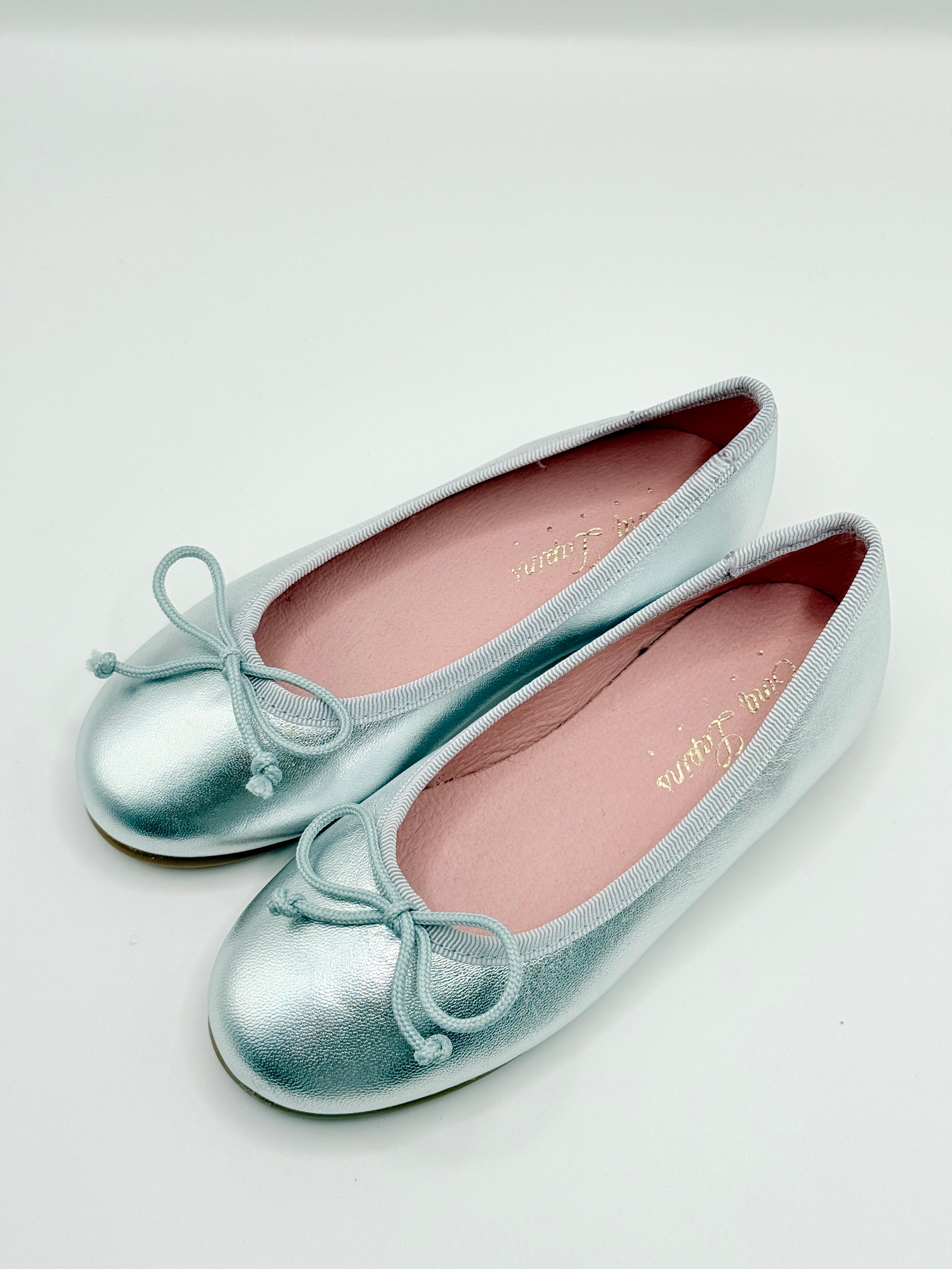 Pair of silver metallic ballet flats with bow details on a light gray background