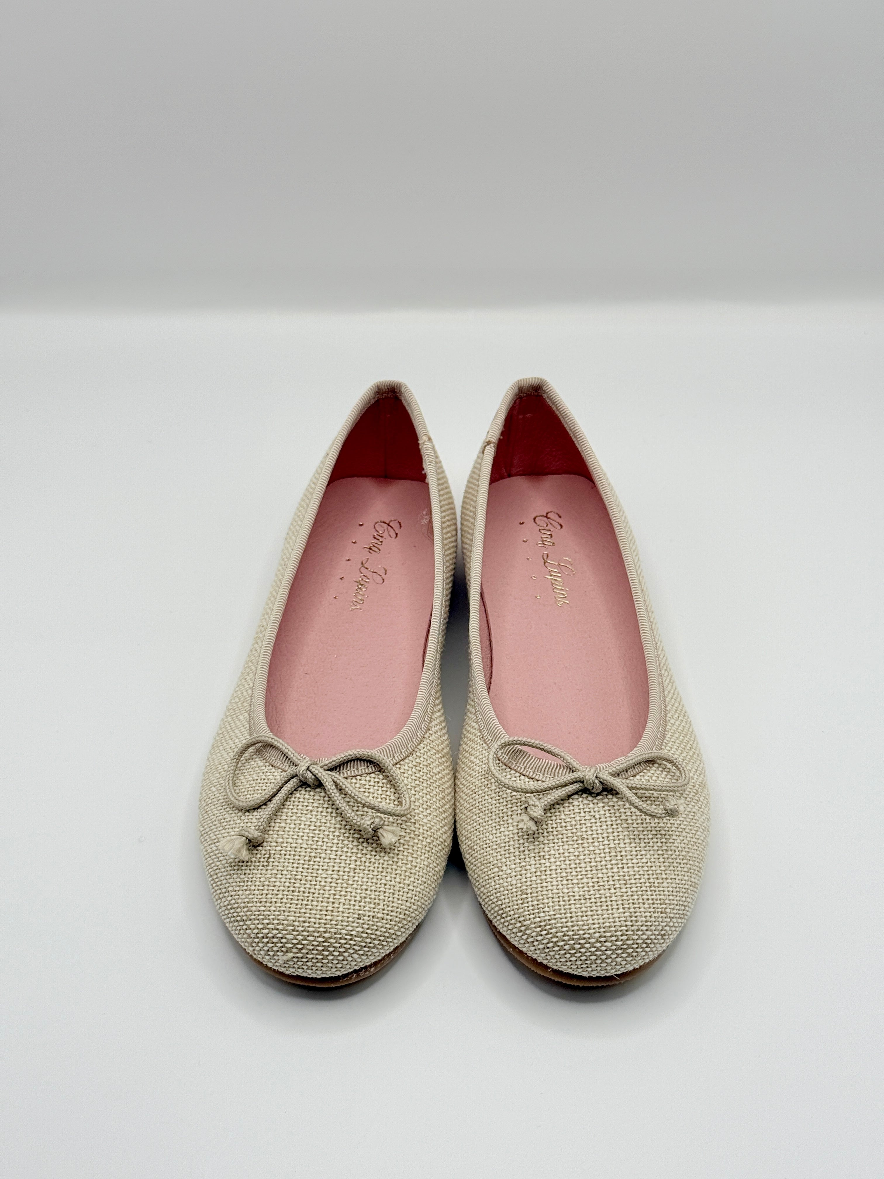 Pair of beige textured shoes with bow details on a white background