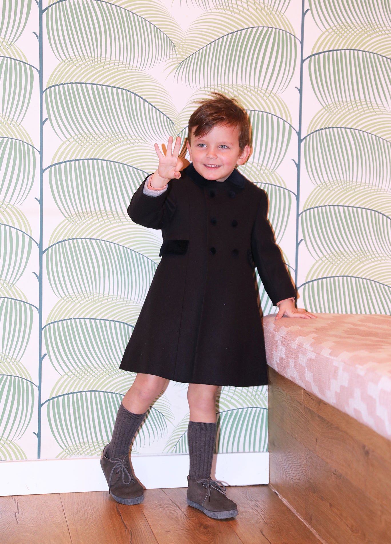 Child wearing a navy coat standing in front of a patterned wall.