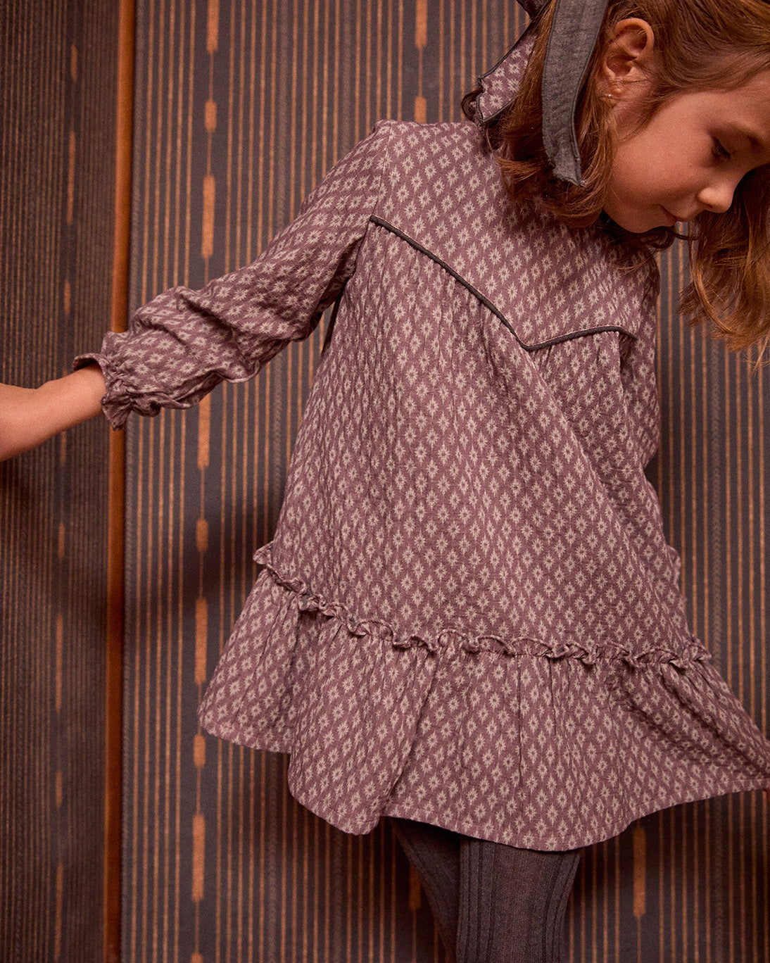 Child wearing a patterned dress against a wooden panel background