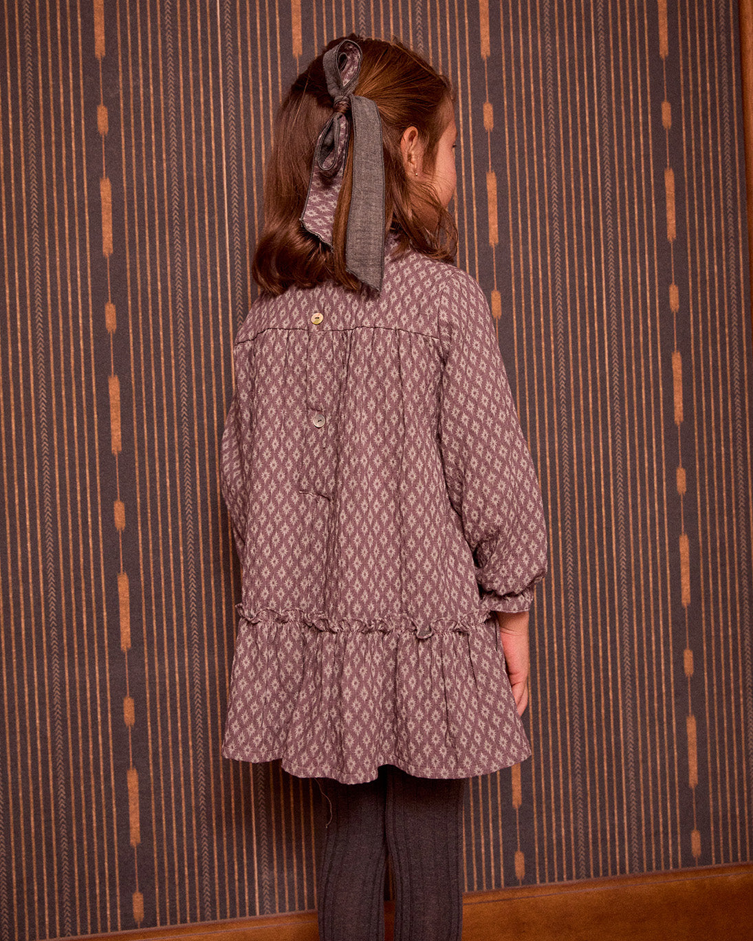 Person wearing a patterned coat standing against a striped wall.