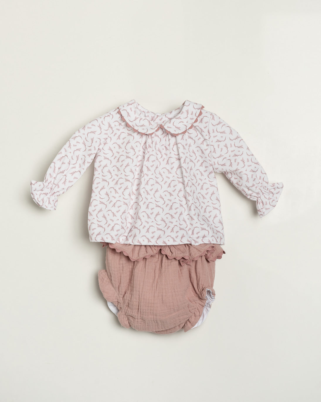 Baby outfit with floral top and pink bloomers on a light beige background