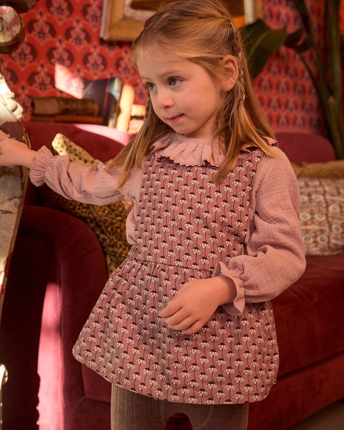 Young girl wearing a pink patterned dress in a room with red and gold decor.