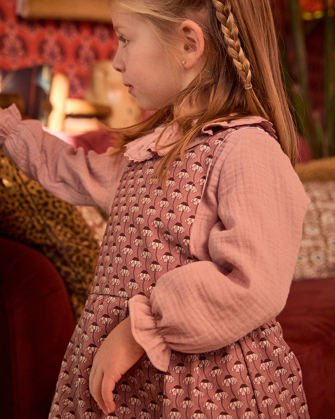 Young girl in a pink dress with a patterned top, standing indoors.