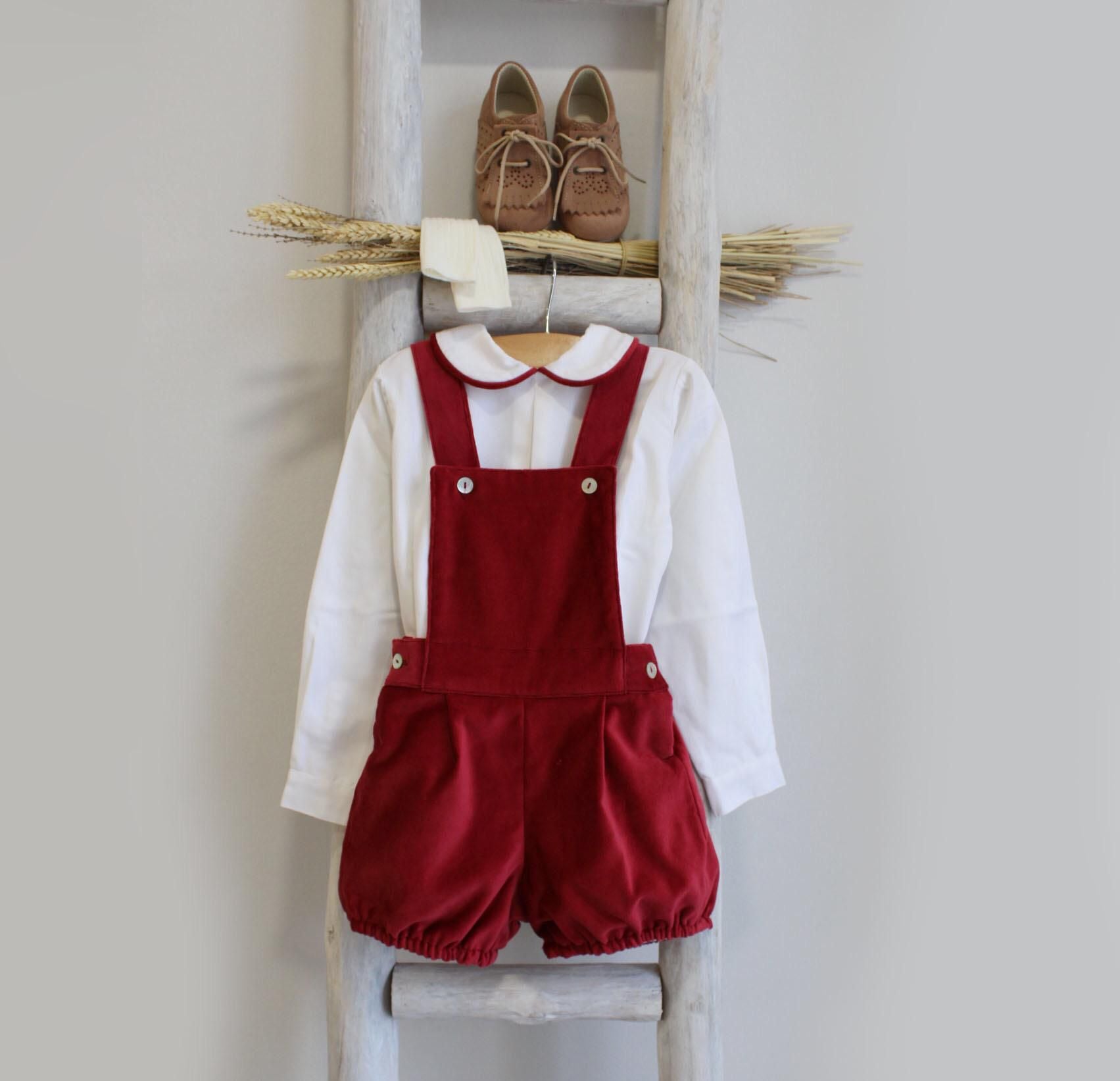 Children's outfit with red overalls and white shirt on a ladder against a light gray wall.
