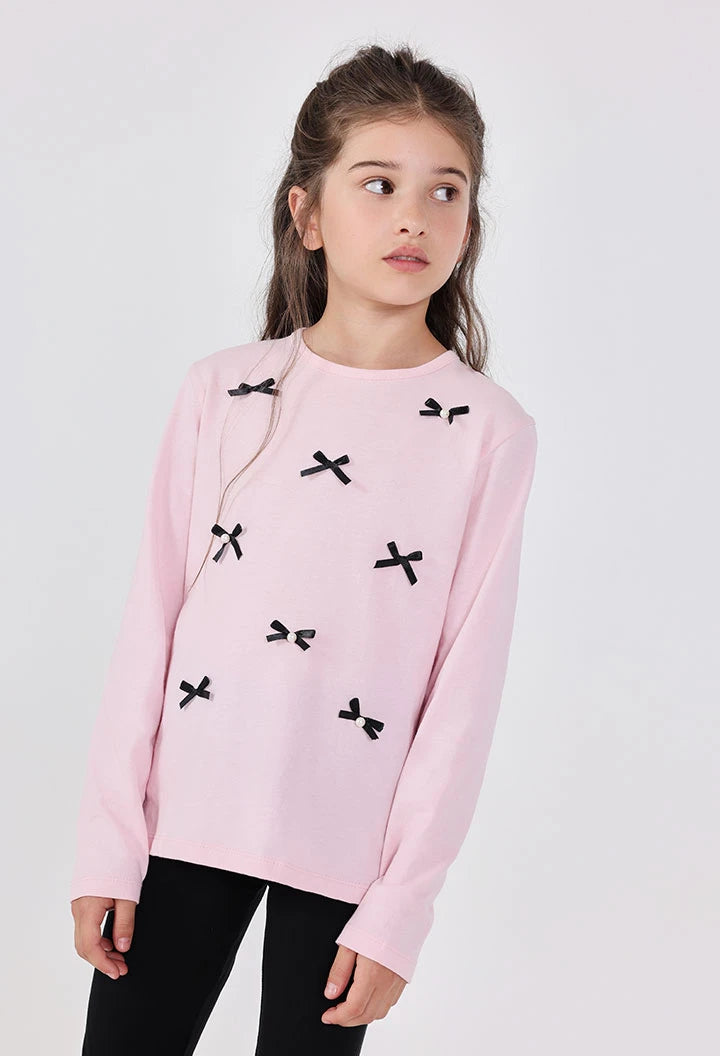 Young girl wearing a pink sweater with black bow patterns on a white background