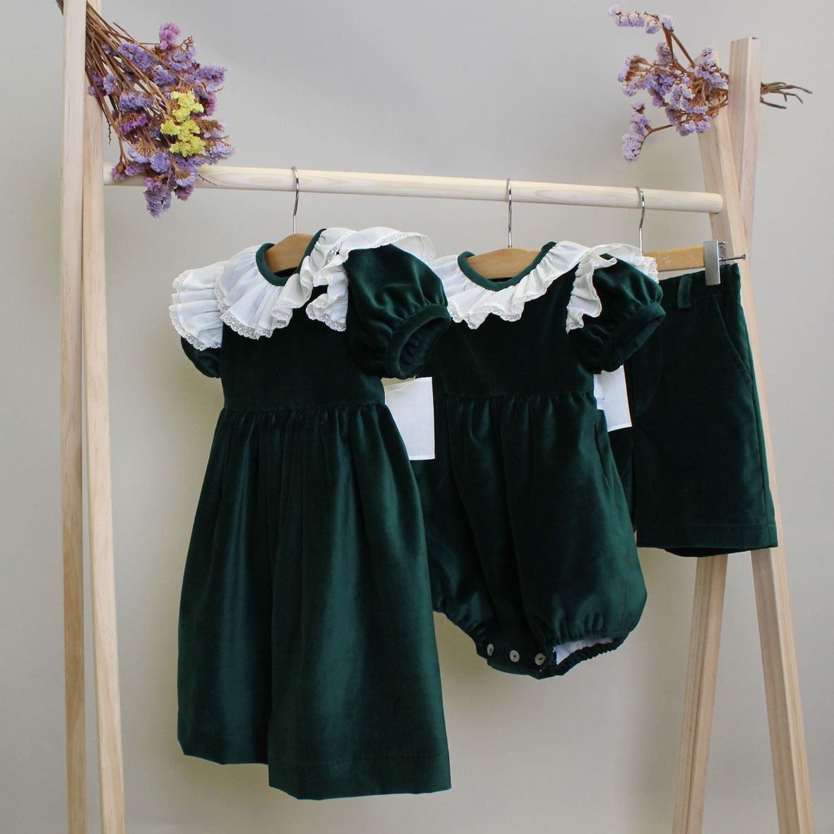 Set of green children's clothing including a dress and romper on a wooden rack.