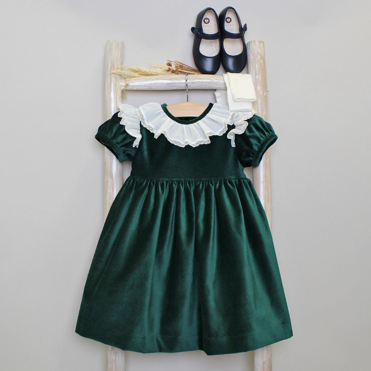Green dress with white ruffled collar on a wooden ladder against a plain background
